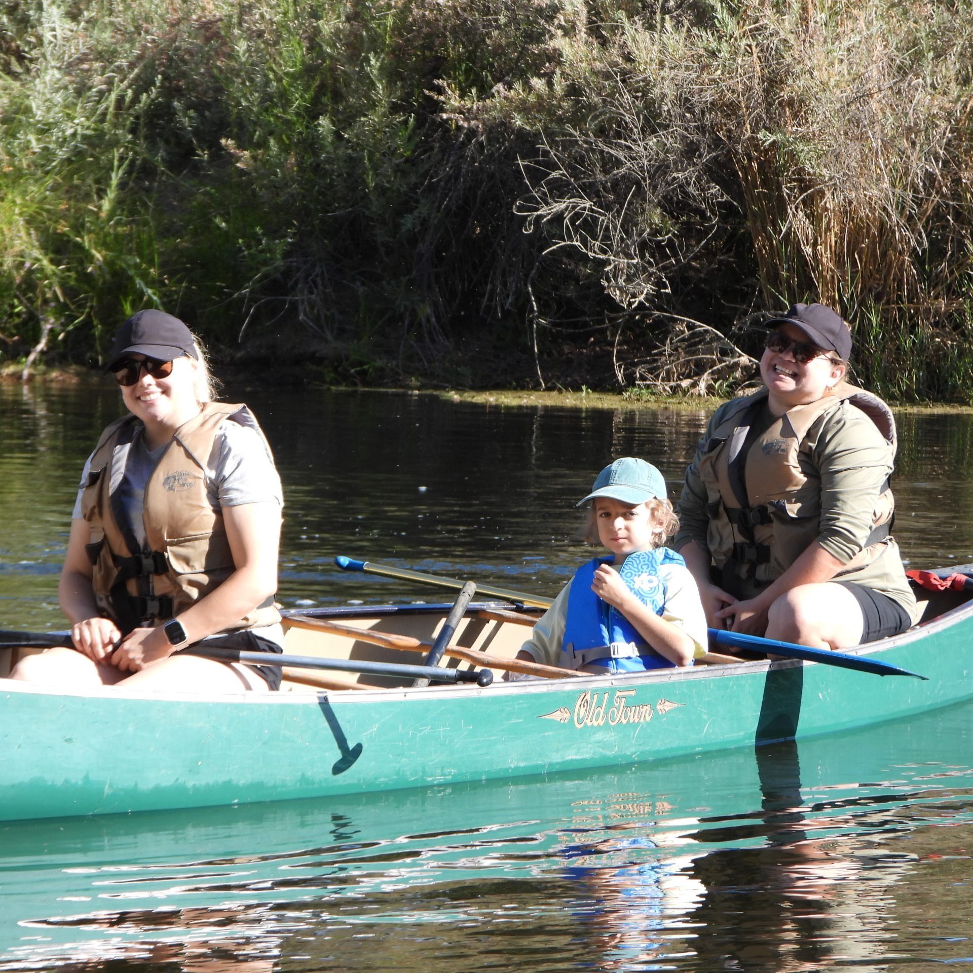 2 adults and a child on a green canoe in the river.
