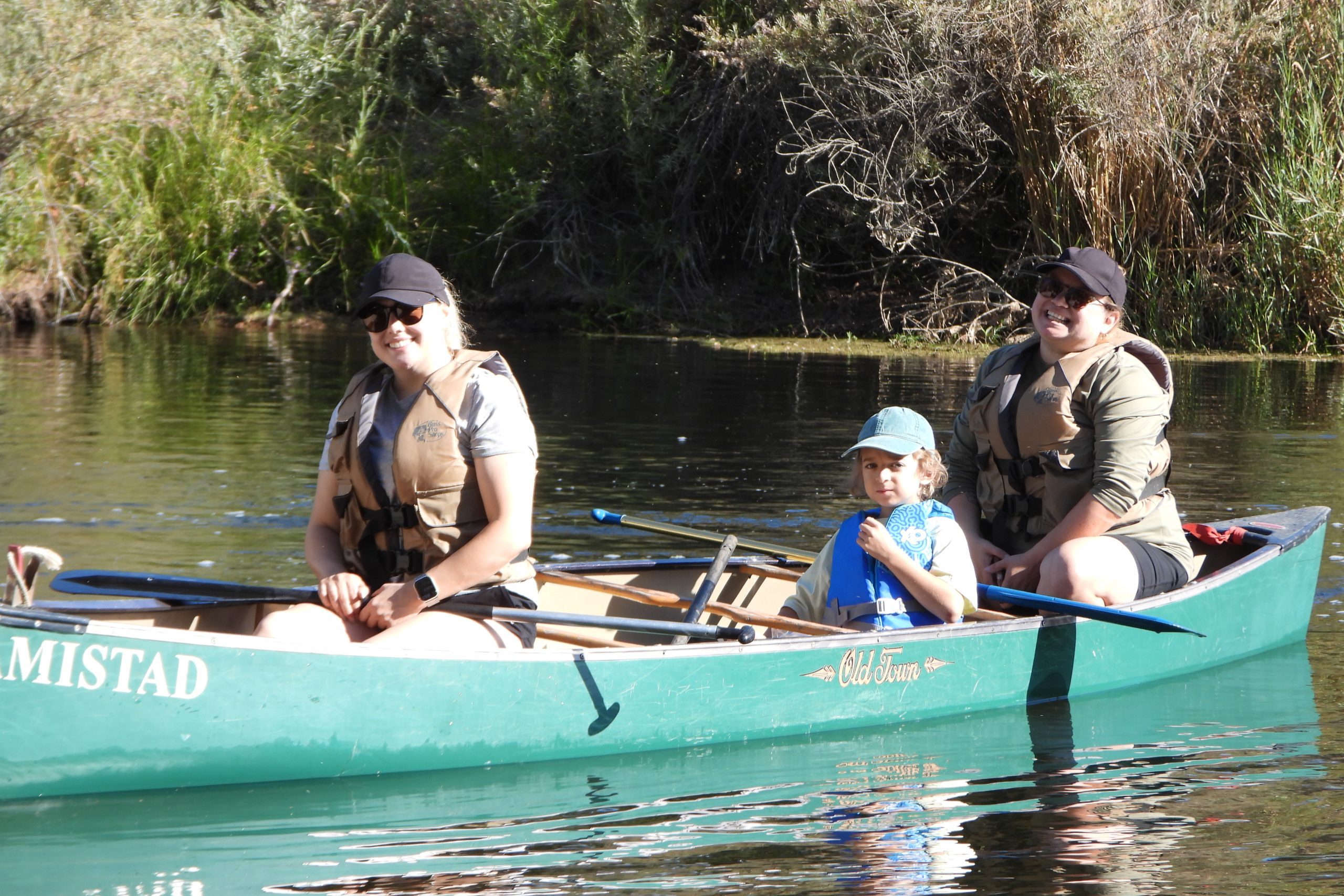 2 adults and a child on a green canoe in the river.